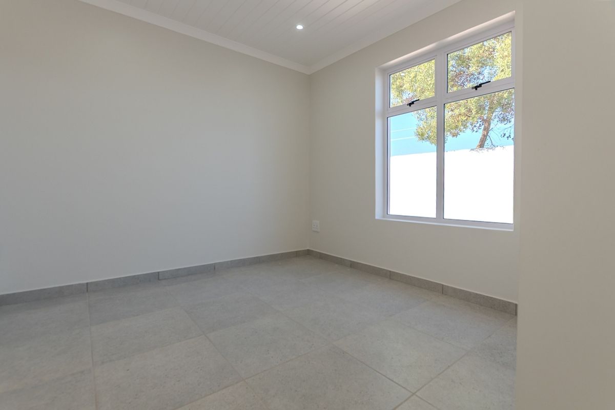 A bright, empty bedroom featuring neutral tiled flooring, a tongue and groove ceiling, and a large window providing natural light.