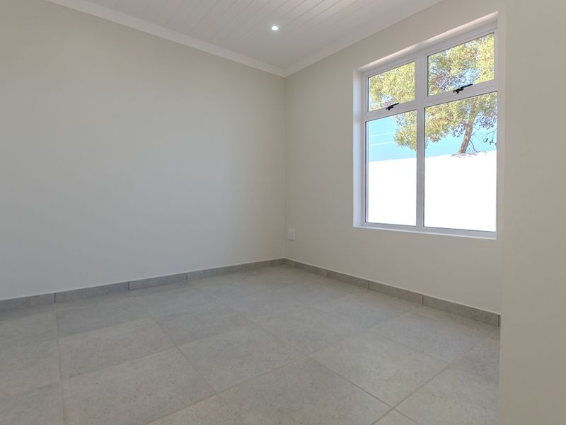 A bright, empty bedroom featuring neutral tiled flooring, a tongue and groove ceiling, and a large window providing natural light.