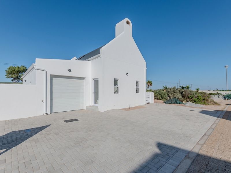 A clean, modern white exterior facade featuring a single garage, paved driveway, and a prominent chimney under a clear blue sky.
