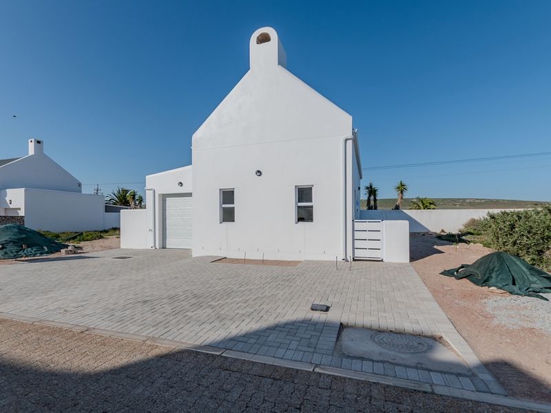 Front view of a white cottage-style house featuring a paved driveway, integrated garage, and chimney, set within a developing residential area.