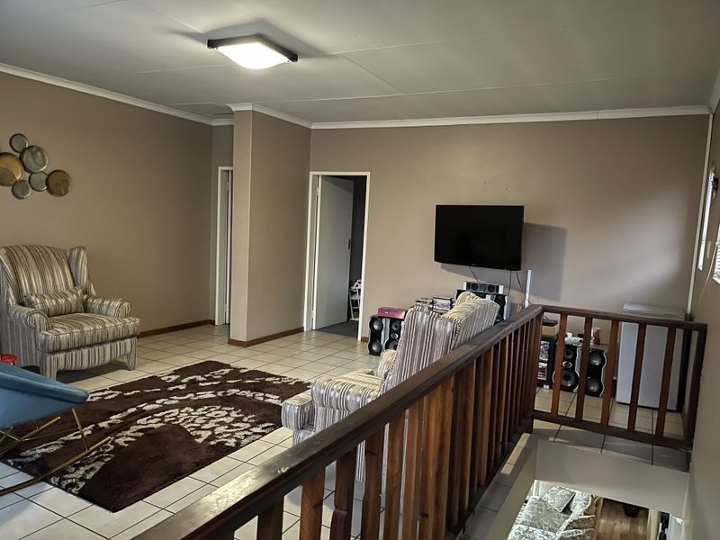A spacious living room featuring tiled flooring, a wooden balustrade overlooking the lower level, and neutral wall finishes.