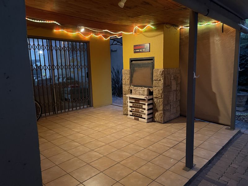 Covered patio area featuring a built-in braai, tiled flooring, and timber ceiling, providing a functional outdoor entertainment space.