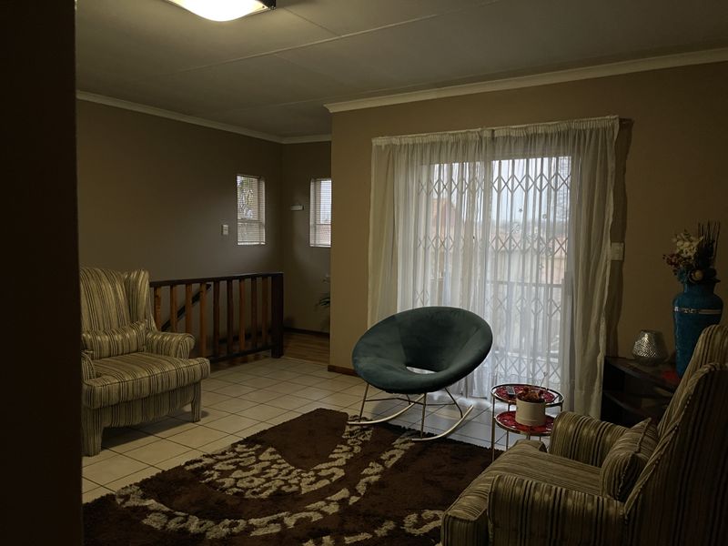 A living room featuring tiled flooring, a sliding glass door with security gate, and access to a staircase area.
