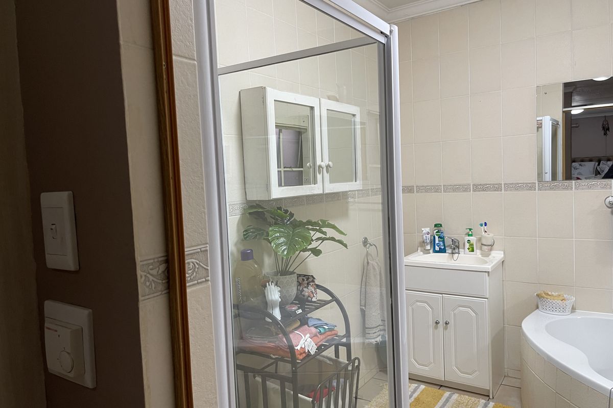 A functional bathroom featuring a corner bathtub, a shower enclosure, a vanity unit with basin, and wall-mounted storage cabinetry with neutral wall tiling.