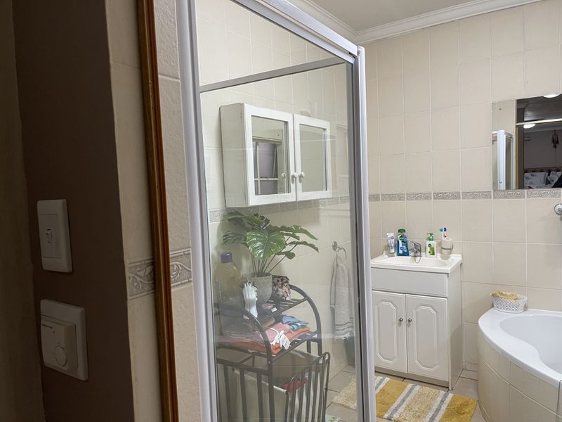 A functional bathroom featuring a corner bathtub, a shower enclosure, a vanity unit with basin, and wall-mounted storage cabinetry with neutral wall tiling.