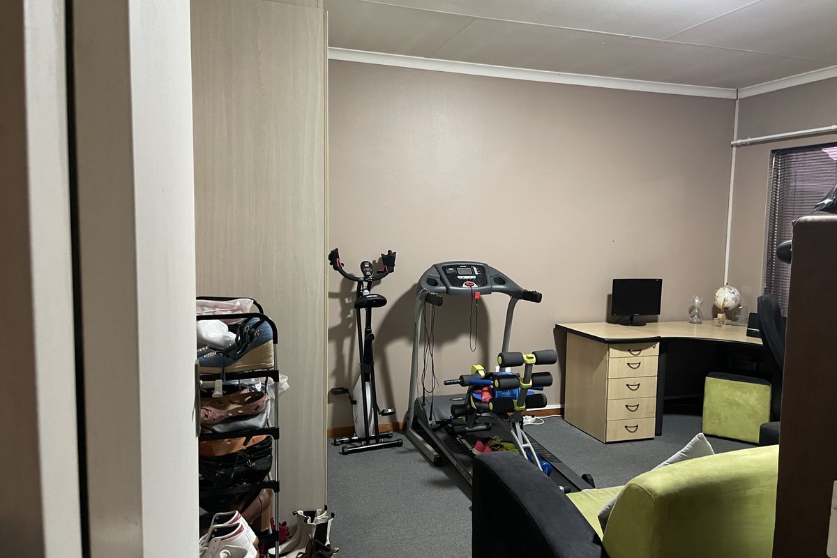 A multi-purpose bedroom featuring built-in cupboards, carpeted flooring, and window blinds, currently utilized as a home office and gym space.