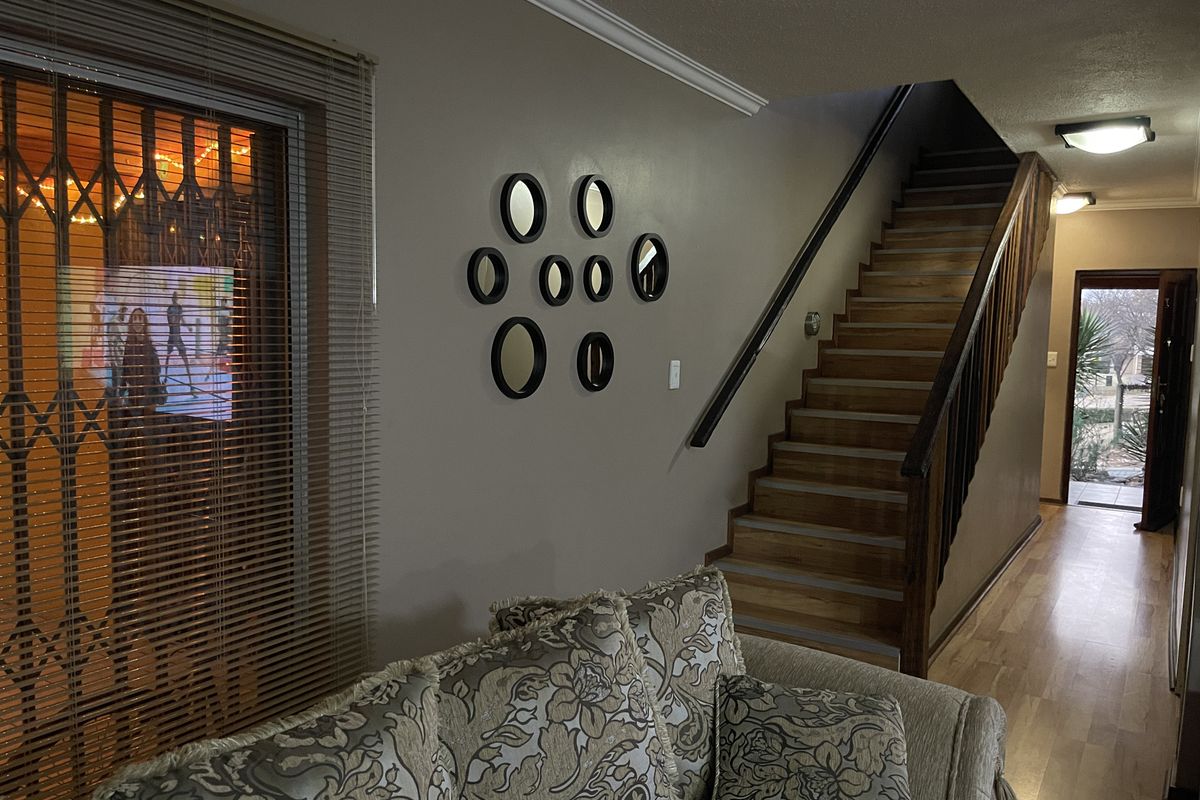 A living area featuring a staircase with a wooden handrail, laminate flooring, and a security gate over the window.