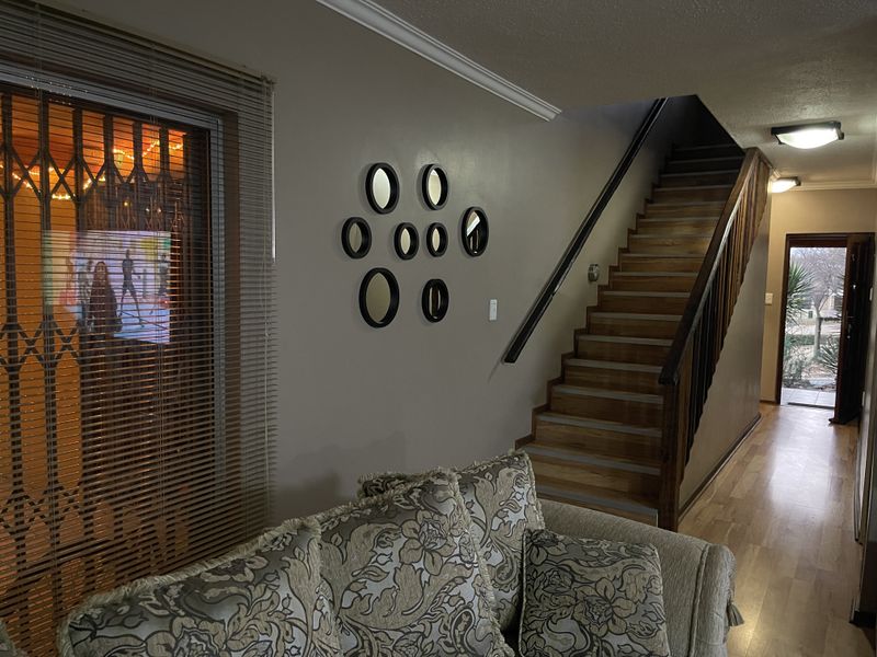 A living area featuring a staircase with a wooden handrail, laminate flooring, and a security gate over the window.