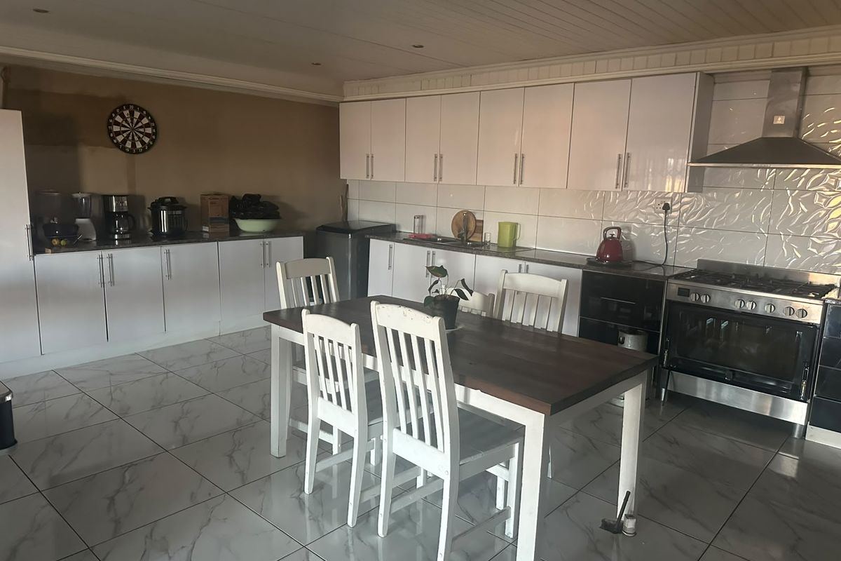 Spacious kitchen featuring white cabinetry, tiled flooring, a gas stove with extractor fan, and a tiled backsplash, offering a functional cooking and dining area.