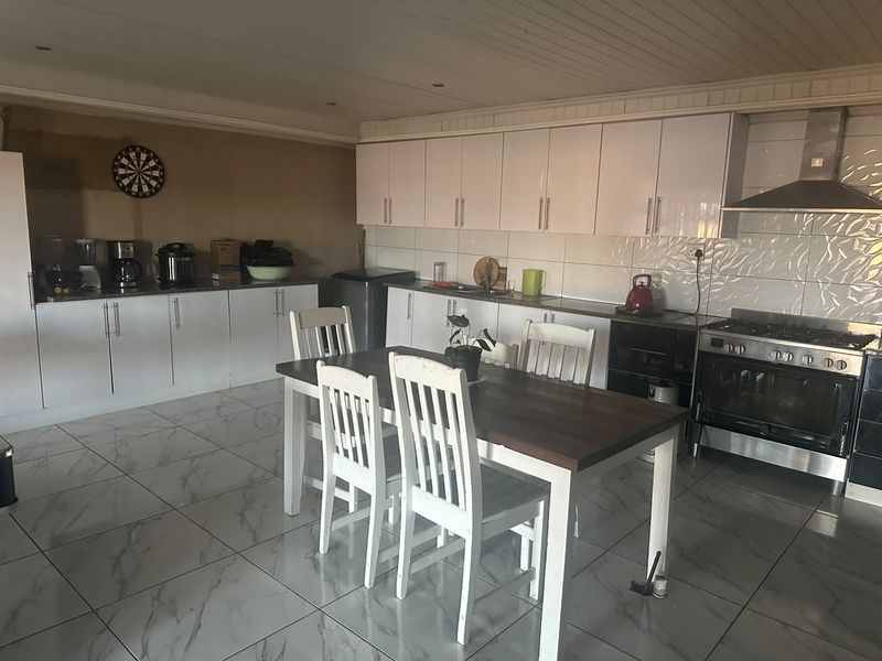 Spacious kitchen featuring white cabinetry, tiled flooring, a gas stove with extractor fan, and a tiled backsplash, offering a functional cooking and dining area.