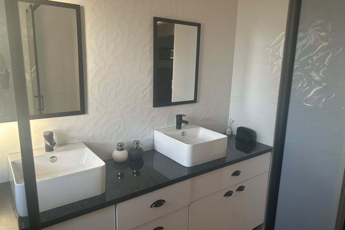 Modern bathroom featuring a double vanity with vessel sinks, granite countertop, and stylish textured wall tiles.
