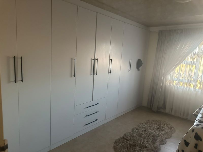 A well-maintained bedroom featuring extensive floor-to-ceiling built-in cupboards with modern hardware and neutral tiled flooring.