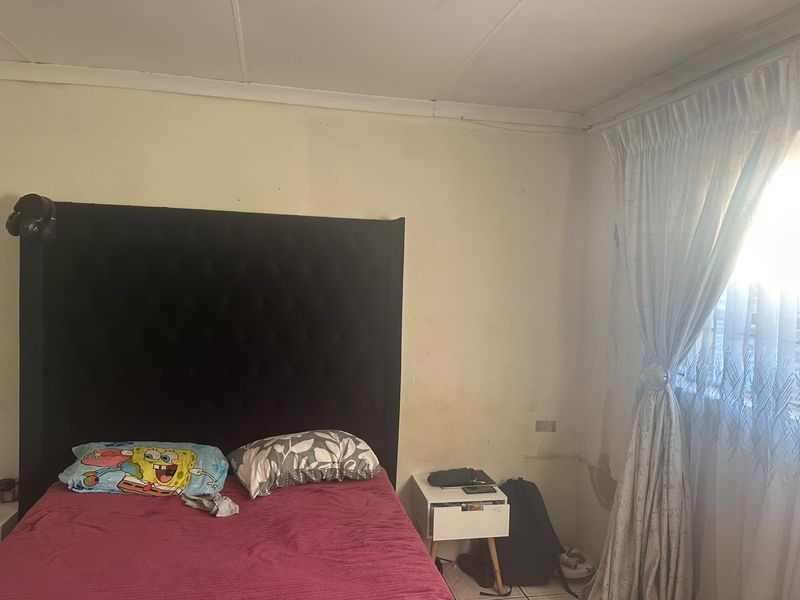 A bedroom featuring tiled flooring and window treatments, currently showing signs of wall staining and ceiling damage requiring maintenance and cosmetic updates.