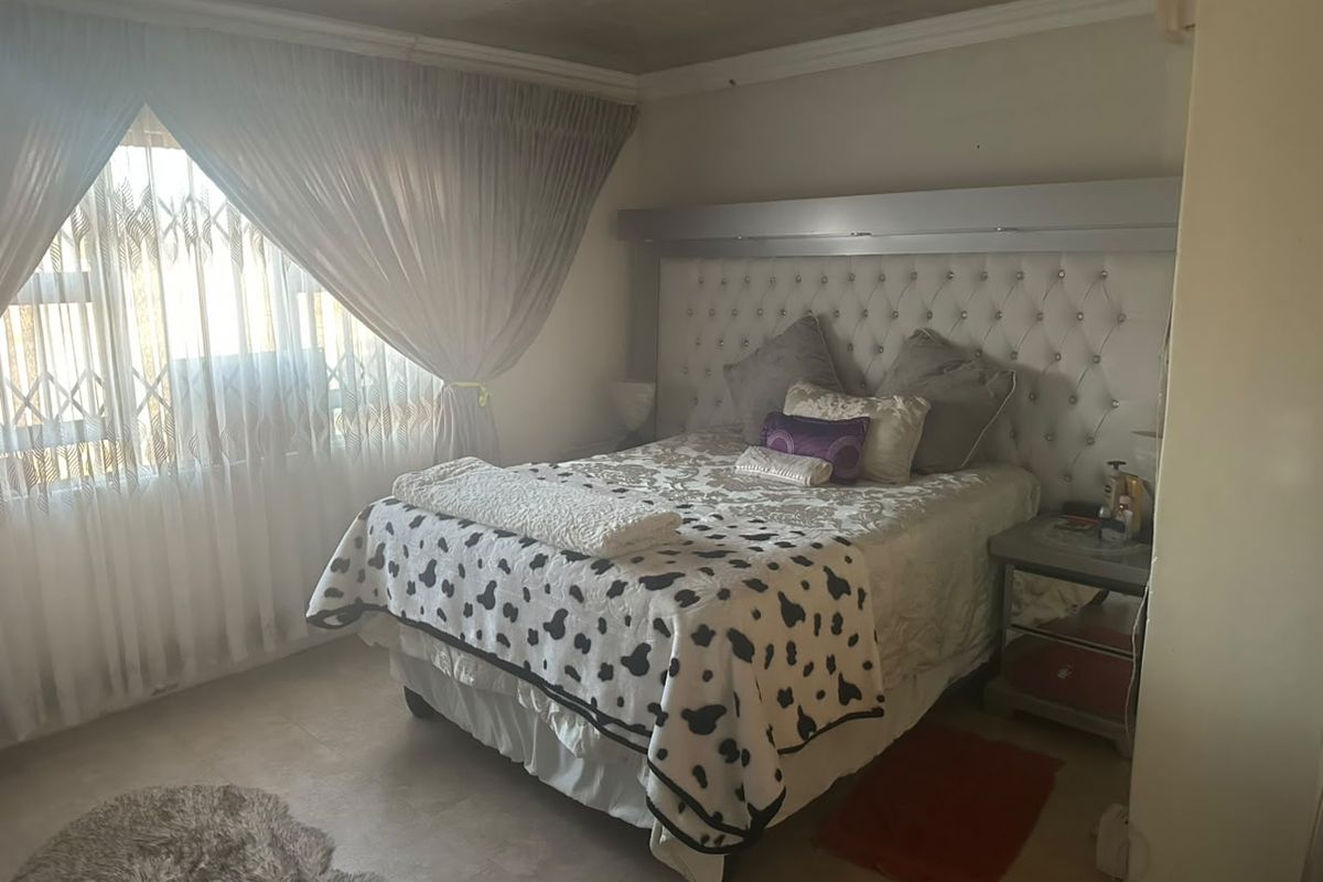 A bedroom featuring a built-in headboard, tiled flooring, and a security gate on the window.