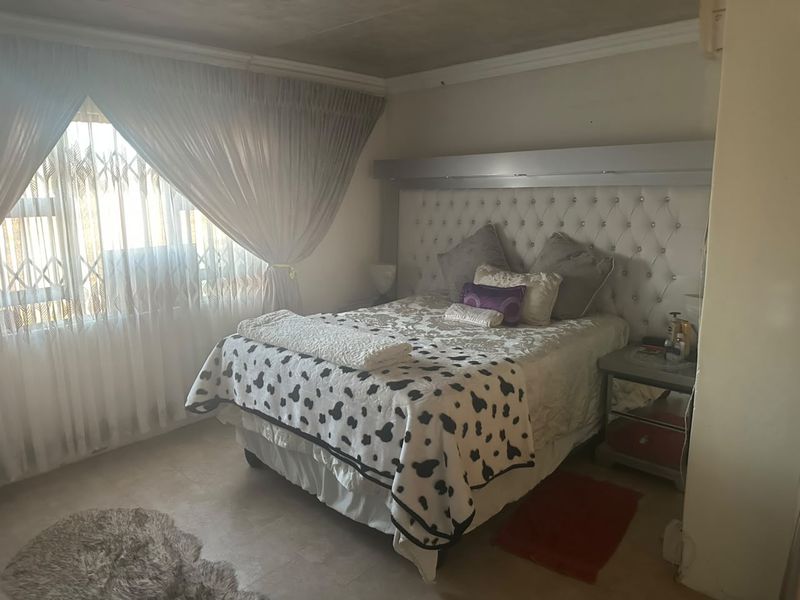 A bedroom featuring a built-in headboard, tiled flooring, and a security gate on the window.