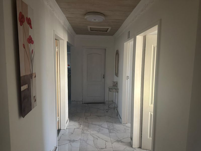 A functional hallway featuring marble-look tiled flooring, a timber-paneled ceiling with decorative cornice, and multiple access points to adjacent rooms.