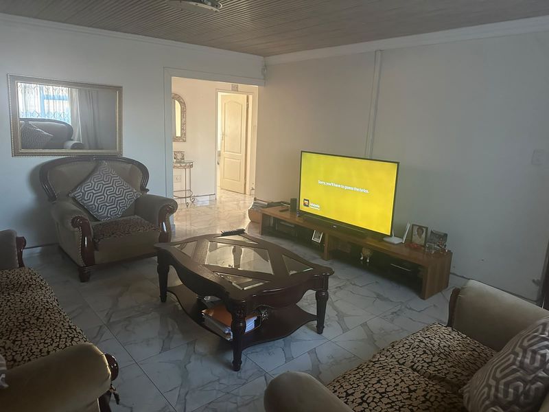 A living room featuring tiled flooring and a timber panelled ceiling, providing a functional space with access to an adjoining hallway.