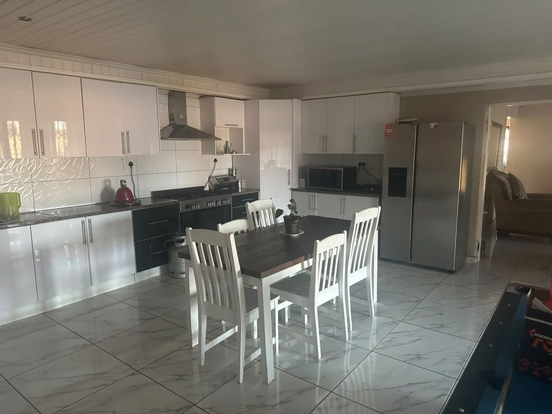Open-plan kitchen and dining area featuring modern white cabinetry, gas hob, extractor fan, and polished marble-look tiled flooring.