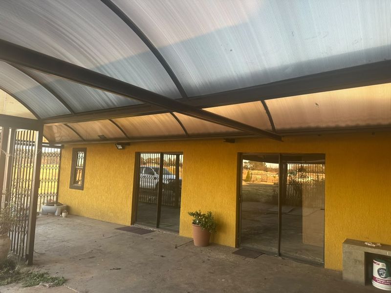 Covered patio area featuring a curved polycarbonate roof, metal support structure, and sliding glass doors providing access to the interior.