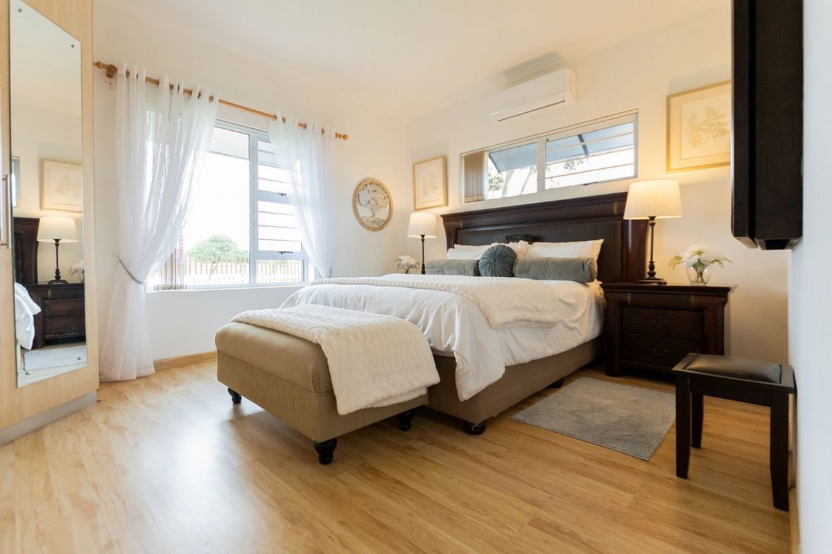 A well-maintained bedroom featuring light laminate flooring, a split-system air conditioner, and large windows allowing for natural light.