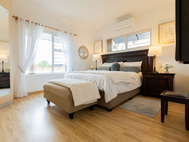 A well-maintained bedroom featuring light laminate flooring, a split-system air conditioner, and large windows allowing for natural light.