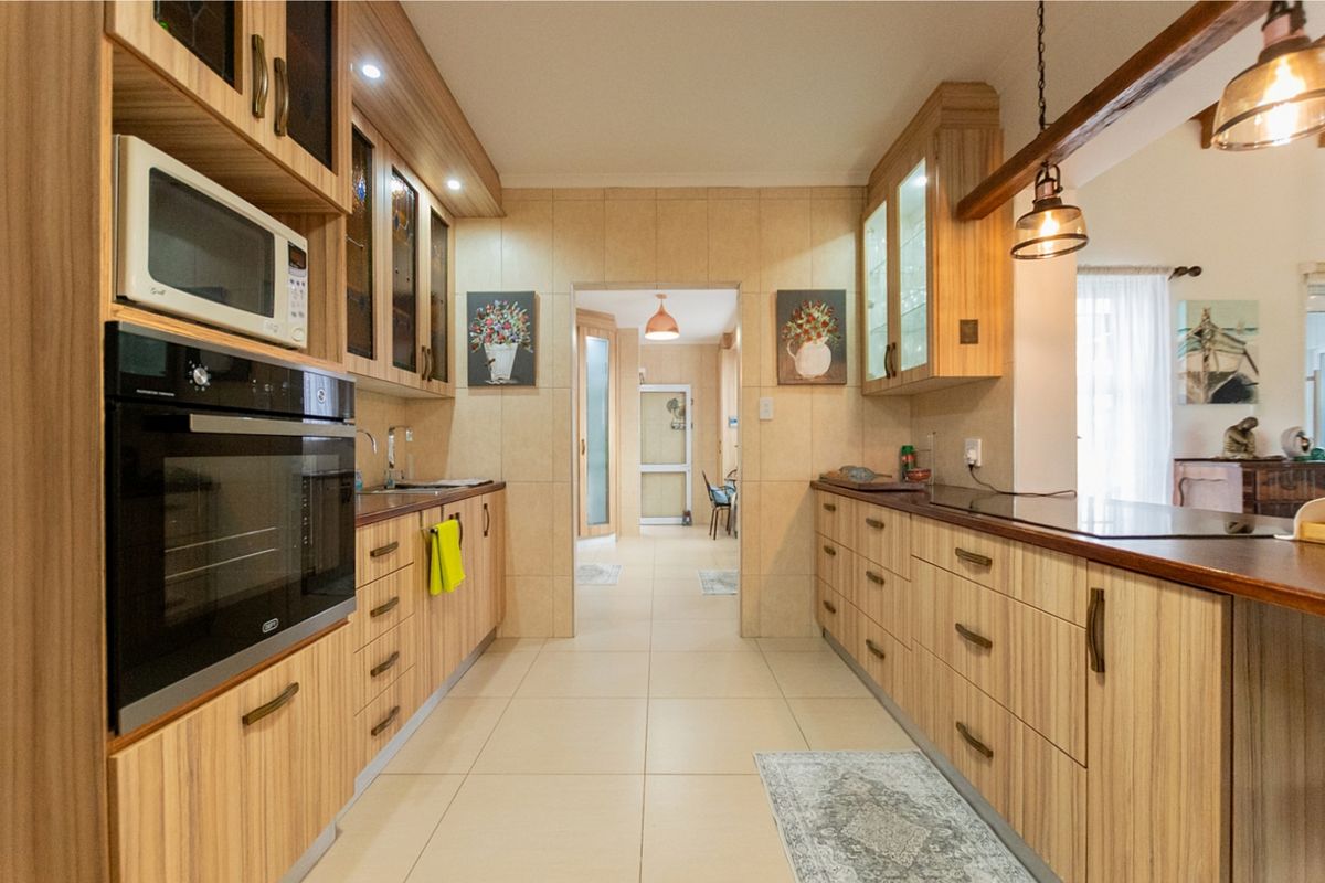 A well-maintained galley-style kitchen featuring light wood-grain cabinetry, built-in oven and microwave, tiled walls, and modern recessed lighting.