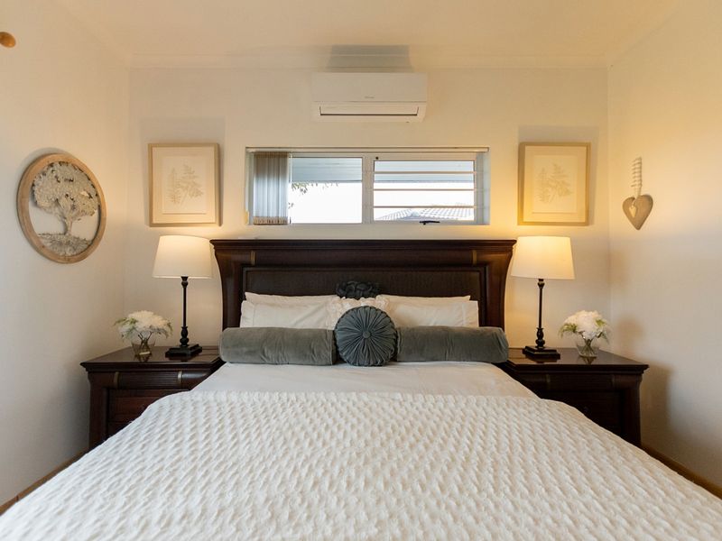 A well-maintained bedroom featuring a wall-mounted split-system air conditioner and a central louvre window above the bed position.