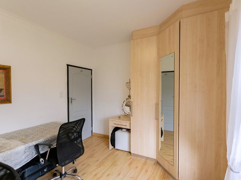 A bedroom featuring light wood-tone laminate flooring and a functional built-in wardrobe with an integrated mirror.