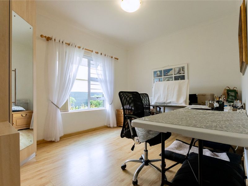A functional bedroom featuring light-toned laminate flooring, a built-in wardrobe with a mirrored door, and a window providing natural light.