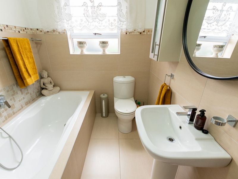 A functional bathroom featuring a bathtub, pedestal basin, toilet, and neutral wall and floor tiling with a wall-mounted medicine cabinet.