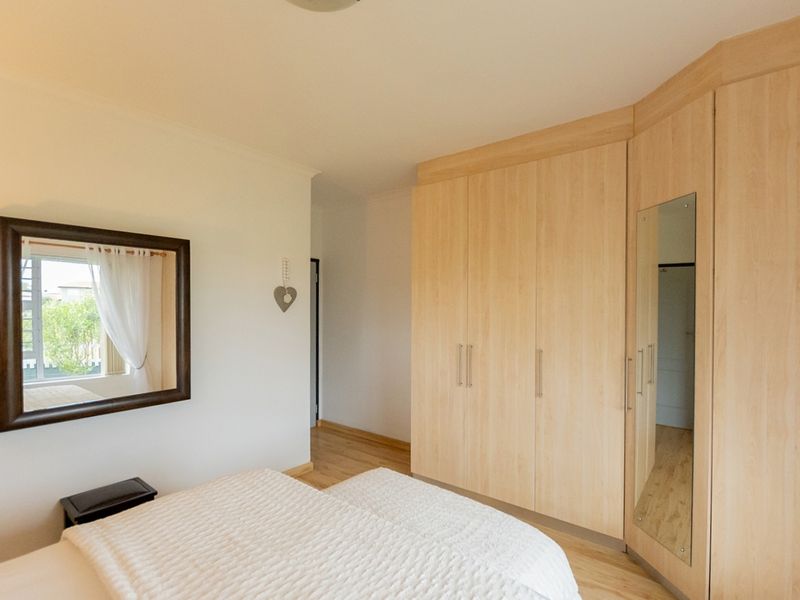 A well-maintained bedroom featuring light wood laminate flooring and extensive built-in cabinetry with an integrated mirror.