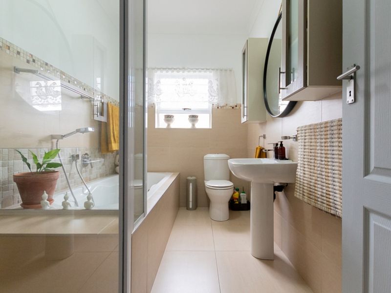 A well-maintained bathroom featuring a pedestal basin, toilet, and a built-in bathtub with a glass shower screen.