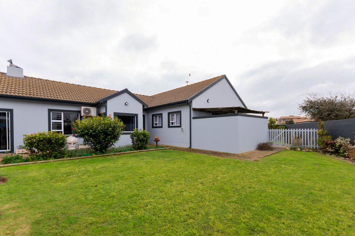 Rear view of the house featuring a well-maintained lawn, paved pathways, and a white picket fence boundary.