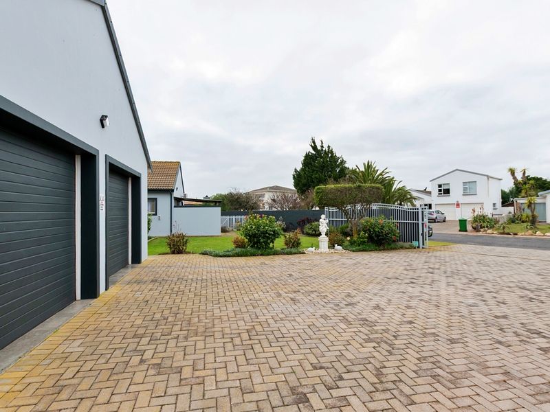 Front view of the property featuring a paved driveway, double garage, and gated entrance with landscaped garden area.
