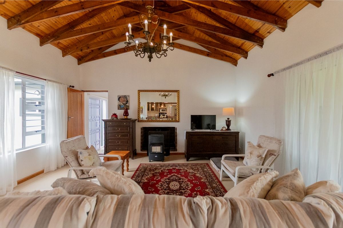Spacious living room featuring a high vaulted ceiling with exposed timber rafters, a central fireplace, and large louver windows allowing for natural light.