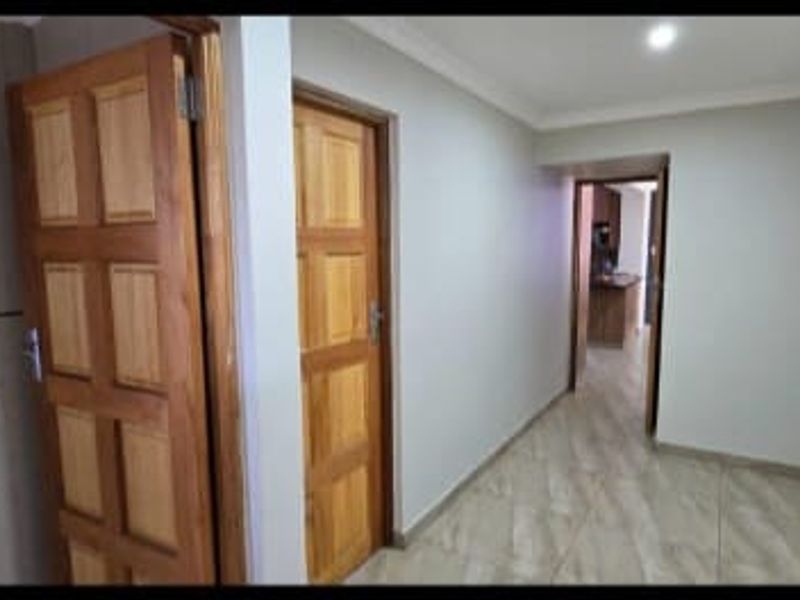 A clean, well-lit hallway featuring tiled flooring and traditional wooden panel doors, providing access to adjacent rooms within the apartment.