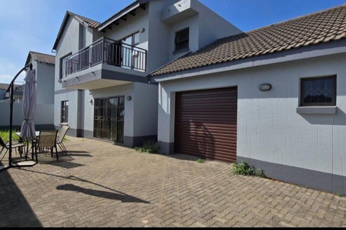 Rear exterior view of the apartment featuring a paved courtyard, single garage, and an upper-level balcony with metal railings.