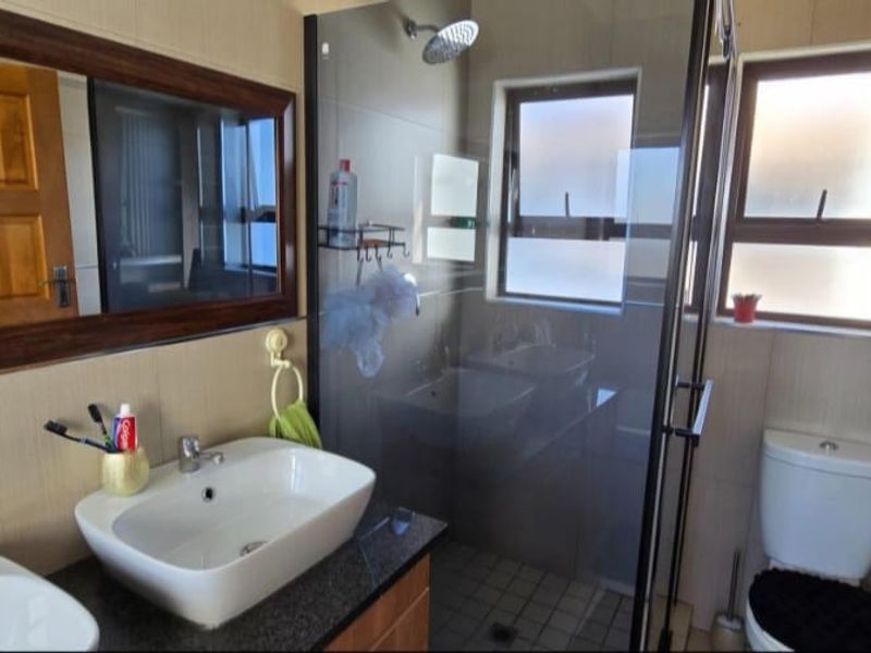 Modern bathroom featuring a double vanity with vessel sinks, a glass-enclosed shower, and neutral wall tiling.