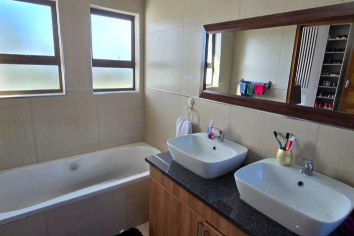 A modern bathroom featuring a double vanity with vessel sinks, granite countertops, and a built-in bathtub with tiled wall finishes.