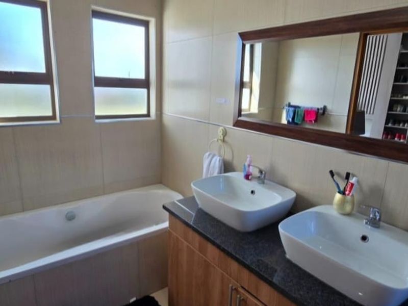 A modern bathroom featuring a double vanity with vessel sinks, granite countertops, and a built-in bathtub with tiled wall finishes.