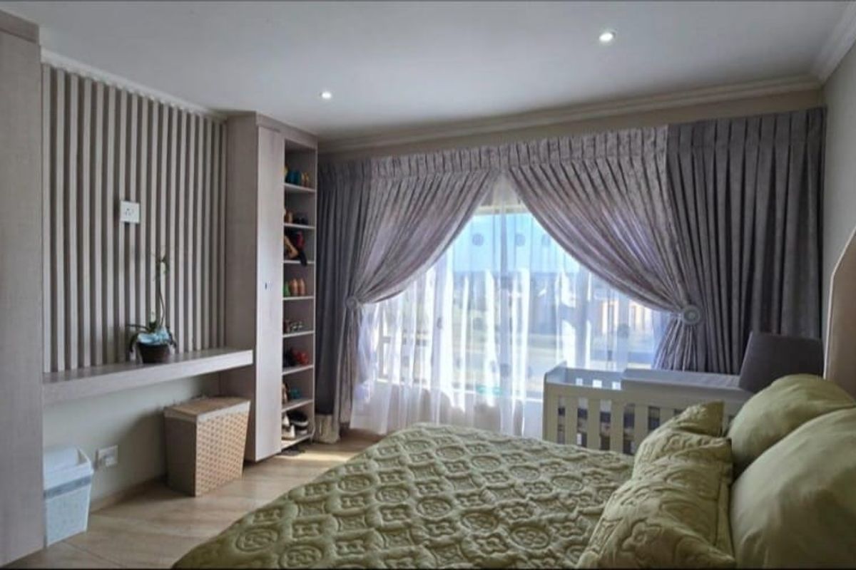 A well-maintained bedroom featuring custom built-in shelving, decorative slatted wall paneling, recessed lighting, and a large window with elegant drapery.
