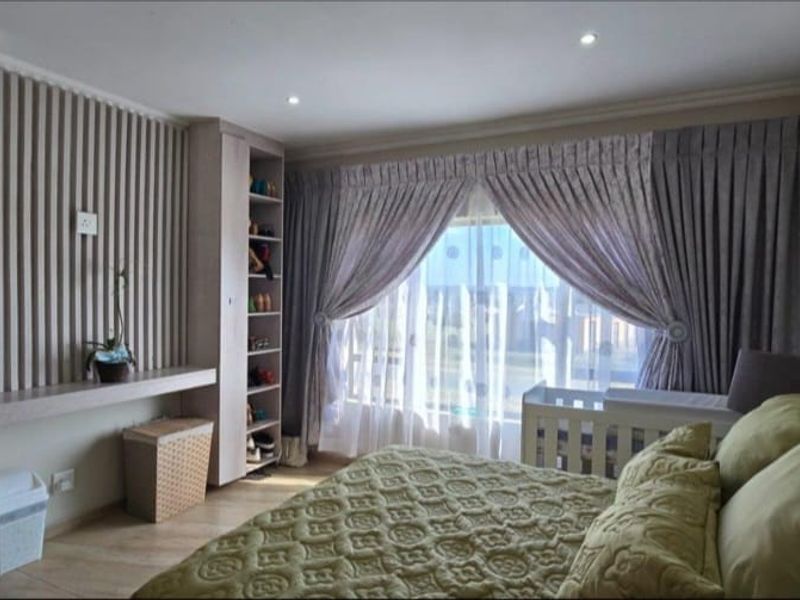 A well-maintained bedroom featuring custom built-in shelving, decorative slatted wall paneling, recessed lighting, and a large window with elegant drapery.