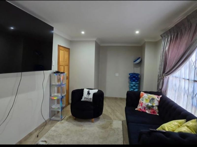 A comfortable living room featuring tiled flooring, recessed downlighting, and a large window fitted with a security gate.