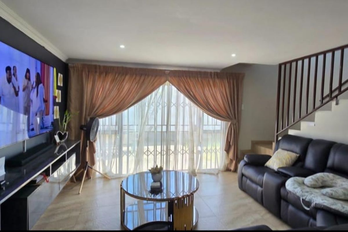A comfortable living room featuring tiled flooring, recessed lighting, and a staircase with a metal balustrade, leading to a sliding glass door with security gate.