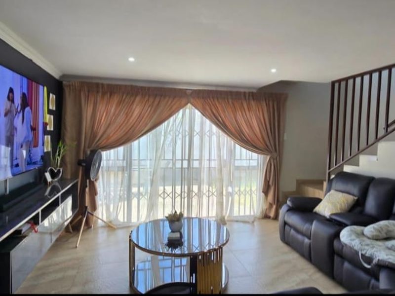 A comfortable living room featuring tiled flooring, recessed lighting, and a staircase with a metal balustrade, leading to a sliding glass door with security gate.
