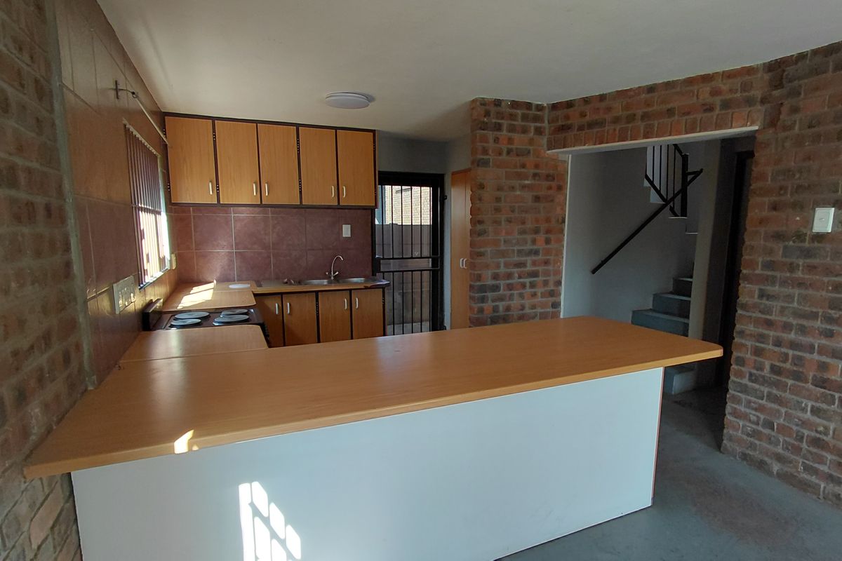 Open-plan kitchen featuring brick walls, built-in cabinetry, a breakfast bar, and an electric hob, with direct access to a rear security door.