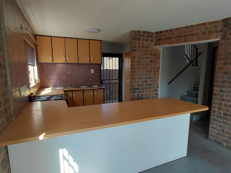 Open-plan kitchen featuring brick walls, built-in cabinetry, a breakfast bar, and an electric hob, with direct access to a rear security door.