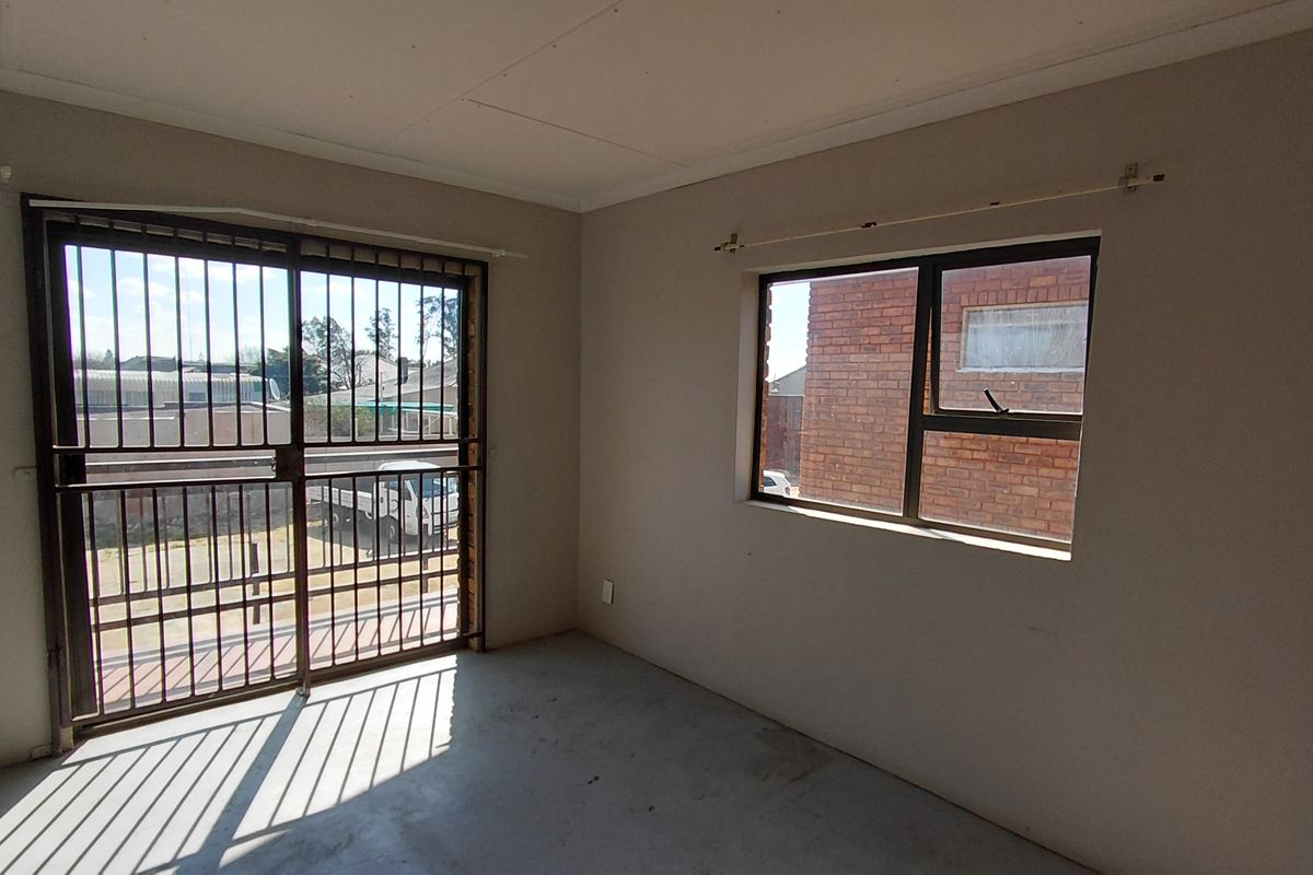 An empty bedroom featuring a sliding security gate and a window with an aluminium frame, offering a blank canvas for potential renovation.