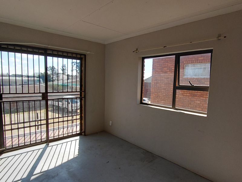 An empty bedroom featuring a sliding security gate and a window with an aluminium frame, offering a blank canvas for potential renovation.