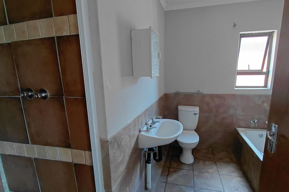 A functional bathroom featuring a shower, bathtub, toilet, and washbasin with neutral tiled finishes.